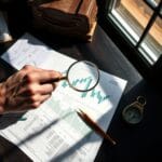 Main tenant une loupe au-dessus d un graphique financier imprime sur un bureau sombre