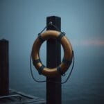 Bouee de sauvetage en laiton accrochee a un poteau de quai avec brume et lueur ambre