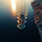 Navire cargo traversant un détroit étroit entre des côtes rocheuses au coucher du soleil