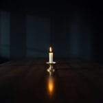 Bougie allumee solitaire dans un bougeoir en laiton sur une grande table sombre et vide