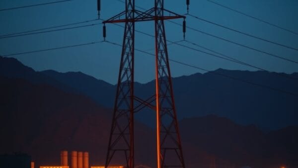 Pylône électrique dans un paysage montagneux au crépuscule avec bâtiments industriels éclairés