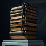 Pile instable de registres financiers en cuir sur socle en marbre entourée d'une chaîne en fer