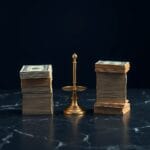 Deux piles de billets sur marbre sombre avec balance en laiton entre les deux