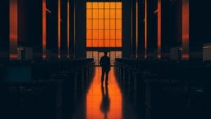Salle de trading vide baignée de lumière ambrée, silhouette lointaine de dos.