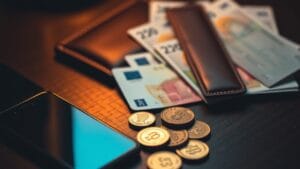 Pièces et billets en euros posés près d'un smartphone et d'une carte de paiement sur un bureau sombre
